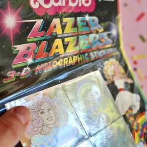 Puede incluir: Un paquete de pegatinas hologr&aacute;ficas 3D Lazer Blazers con un dise&ntilde;o de arco&iacute;ris. Las pegatinas son hologr&aacute;ficas y tienen un efecto arco&iacute;ris.