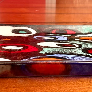 Könnte beinhalten: Ein quadratisches Serviertablett aus Glas mit schwarzem Hintergrund und einem farbenfrohen abstrakten Design. Das Design zeigt Wirbel in Rot, Orange, Gelb, Grün, Blau und Weiß.
