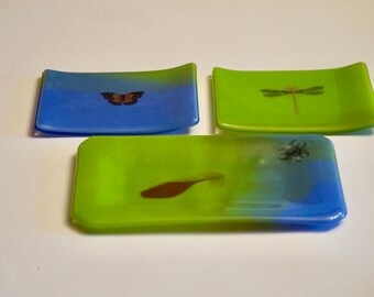 Könnte beinhalten: Drei kleine, rechteckige Glasschalen mit einem blauen und grünen Ombre-Design. Jede Schale zeigt ein anderes Insekt: einen Schmetterling, eine Libelle und eine Spinne.