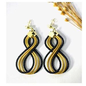 May include: A pair of gold and black infinity symbol earrings. The earrings are made of braided cords and have a gold hook closure.