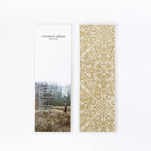 May include: A white bookmark with a brown patterned design on the right side. The left side features the text "evermore album Taylor Swift" in black.