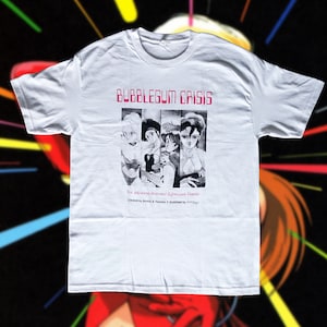 Puede incluir: Camiseta blanca con un diseño gráfico de la serie de anime Bubblegum Crisis. El diseño incluye el título de la serie en rosa y una ilustración en blanco y negro de varios personajes. La camiseta tiene cuello redondo.