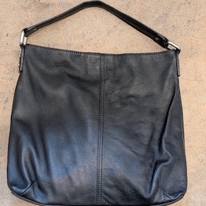 May include: A black leather hobo bag with a single shoulder strap, silver-toned metal hardware, and a vertical stitched seam running down the center of the front panel. The bag features a textured surface and a slouchy, unstructured silhouette.