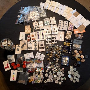 May include: A large collection of assorted sewing buttons in various shapes, sizes, and colors, including packaged sets on cardboard backing, loose buttons in a glass jar, plastic bags, and a blue container, featuring alphabet and decorative designs.