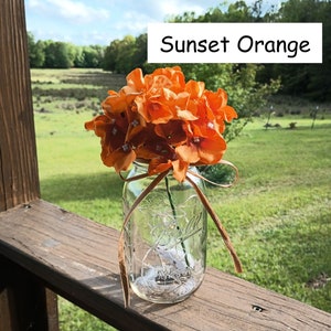 May include: A mason jar filled with a bouquet of orange silk flowers, tied with a brown ribbon. The jar is sitting on a wooden surface. The text "Sunset Orange" is visible in the image.