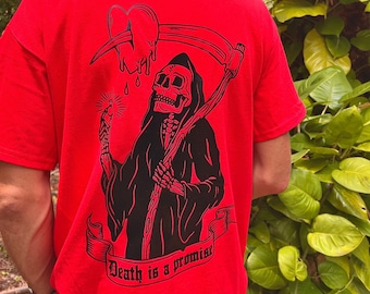 May include: Red t-shirt with a black graphic of a skeleton holding a scythe and a heart. The text "Death is a promise" is printed on a banner below the skeleton.