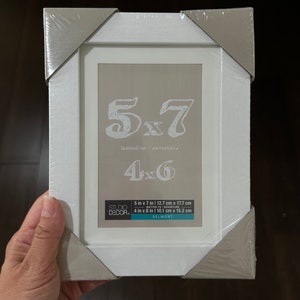 May include: White picture frame with a silver border. The frame is packaged and ready to be used. The frame is designed to fit a 5x7 inch photo, but can also be used for a 4x6 inch photo. The frame is made by Studio Decor and is called Belmont.