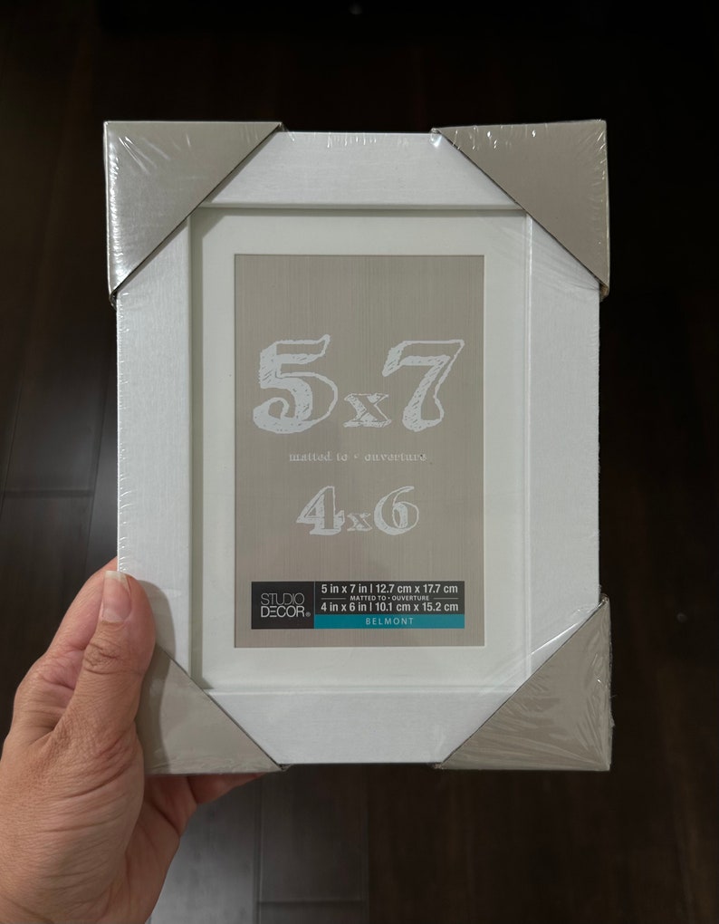 May include: White picture frame with a silver border. The frame is packaged and ready to be used. The frame is designed to fit a 5x7 inch photo, but can also be used for a 4x6 inch photo. The frame is made by Studio Decor and is called Belmont.