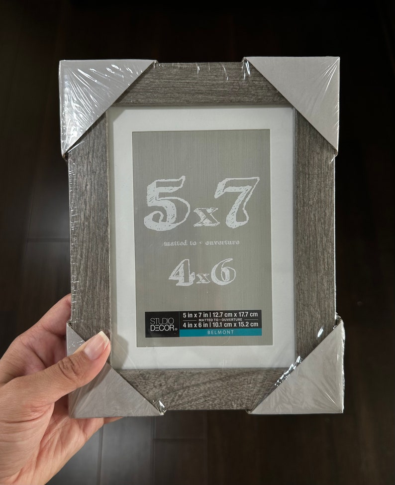 May include: A gray wood picture frame with a white mat. The frame is labeled "5x7 matted to ouverture 4x6". The frame is 5 inches by 7 inches and can fit a 4 inch by 6 inch photo.