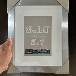 May include: Silver picture frame with a white mat and a clear glass front. The frame is designed to hold an 8x10 inch photo, but can also be used to display a 5x7 inch photo with a mat. The frame has the text "8x10 matted to ouverture 5x7" printed on the front.
