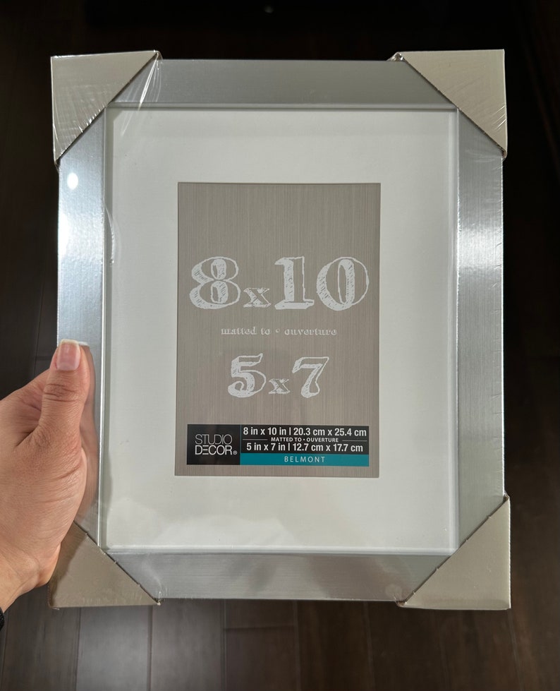 May include: Silver picture frame with a white mat and a clear glass front. The frame is designed to hold an 8x10 inch photo, but can also be used to display a 5x7 inch photo with a mat. The frame has the text "8x10 matted to ouverture 5x7" printed on the front.