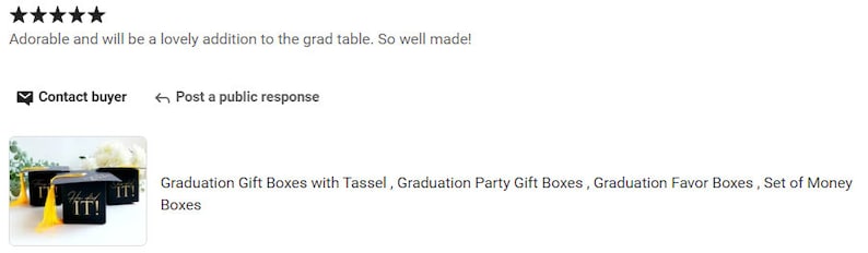K&ouml;nnte beinhalten: Satz von drei schwarzen Geschenkboxen zum Abschluss mit goldenen Quasten und dem Text "IT!" auf der Vorderseite. Die Boxen stehen auf einem Tisch mit gr&uuml;nen Pflanzen im Hintergrund.