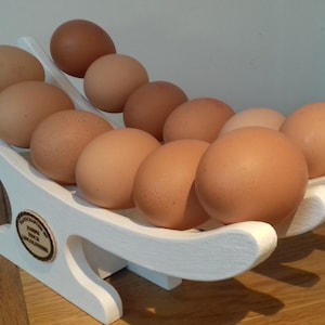 May include: White wooden egg holder with a curved design, holding a dozen brown eggs.