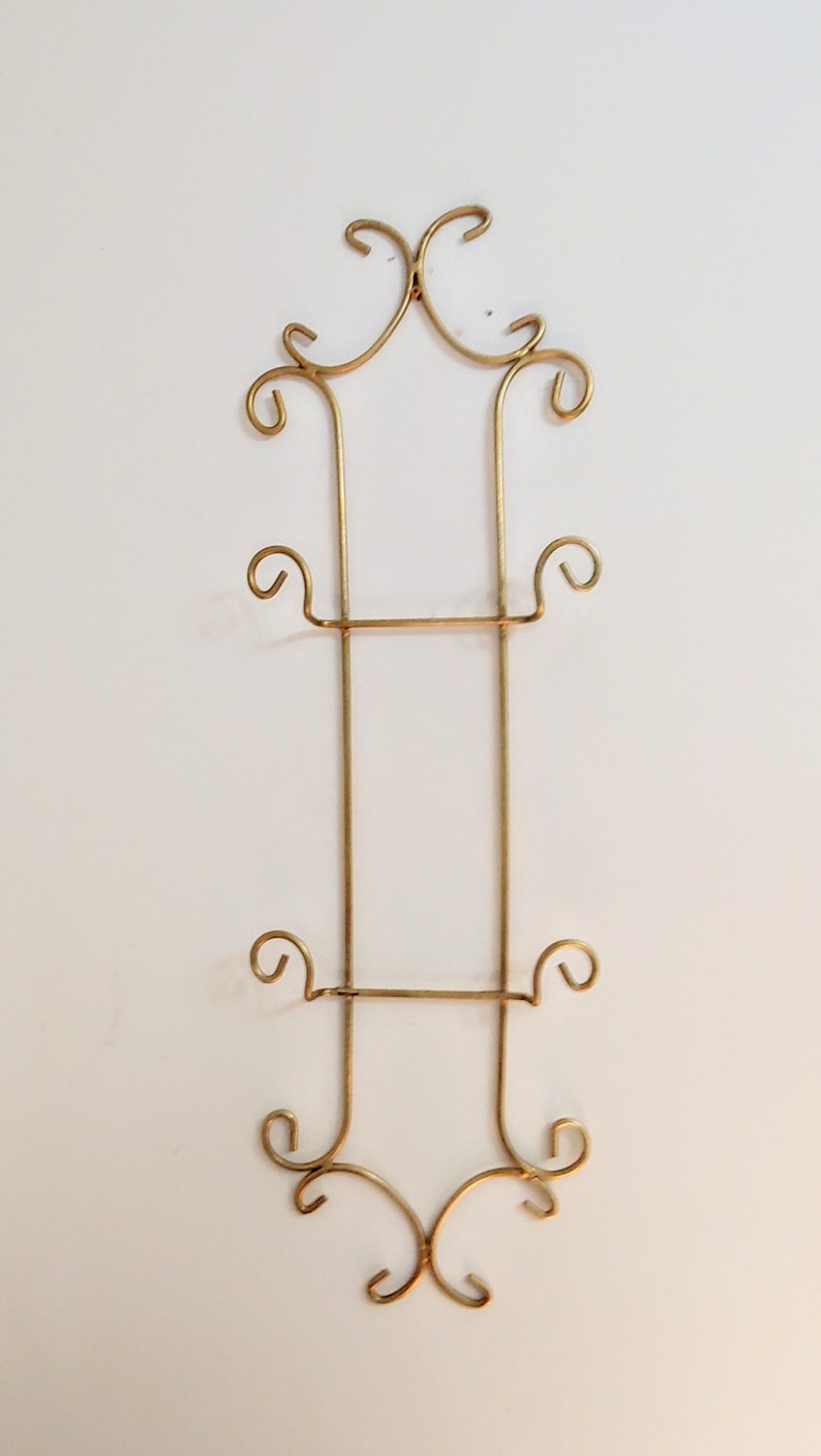 May include: Gold metal plate holder with three tiers and decorative scrollwork at the top and bottom.