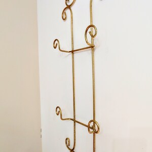 May include: Gold metal wall mounted plate rack with decorative scrollwork. The rack has three tiers for displaying plates.