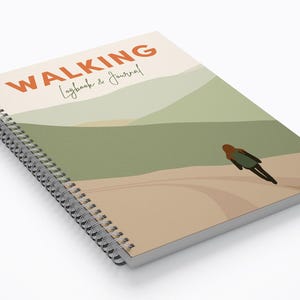 May include: A spiral bound notebook with a colourful abstract landscape design on the cover. The cover features a person walking on a path with a mountain range in the background. The title "WALKING Logbook & Journal" is printed in orange on the cover.