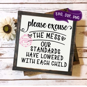 May include: A black and white sign with the text "please excuse the mess our standards have lowered with each child". The sign is on a wooden background.