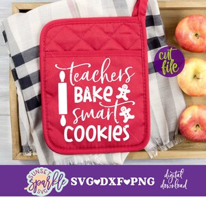 Może przedstawiać: Czerwona rękawica do piekarnika z białym tekstem, który brzmi "Teachers bake smart cookies". Tekst zawiera grafikę wałka do ciasta i piernikowych ludzików. Rękawica do piekarnika znajduje się na drewnianej tacy z tkaniną w kratkę i czerwonymi jabłkami.