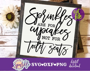 May include: A framed wooden sign with the text "Sprinkles are for cupcakes not for toilet seats" in black script. The sign has a white background and a dark brown frame. A decorative sunflower is in the upper left corner.