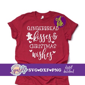Può includere: Maglietta rossa con testo bianco che recita "Gingerbread Kisses & Christmas Wishes". Un'icona di gingerbread man è accanto alla parola "Kisses".