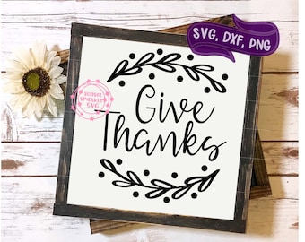 Puede incluir: Un letrero en blanco y negro con un marco de madera rústico. El letrero dice "Give Thanks" con una corona decorativa alrededor del texto.