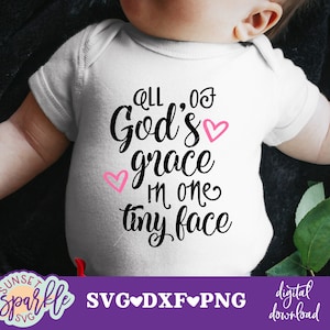 May include: White baby onesie with black text that reads "All of God's grace in one tiny face". There are two pink hearts in the design.