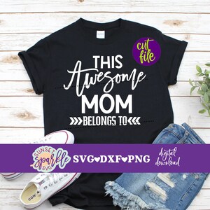 May include: A black t-shirt with white text that reads "This Awesome Mom Belongs To". The shirt is laid flat on a wooden surface with a pair of white sneakers and denim shorts.