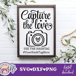 Może przedstawiać: Oprawiony znak z napisem "Capture the love" nad ilustracją aparatu. Poniżej aparatu znajduje się "USE THE HASHTAG #YourHashTagHere". Znak ma wymiary 35,56 x 48,26 cm i ma ciemnobrązową ramę.