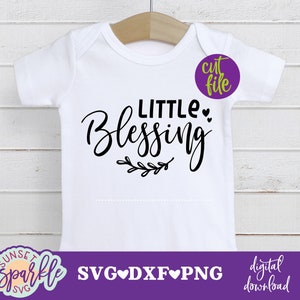 Könnte beinhalten: Ein weißer Baby-Strampler mit schwarzem Text, der "Little Blessing" lautet, mit einem kleinen floralen Design darunter. Der Text ist in einer kursivschrift.