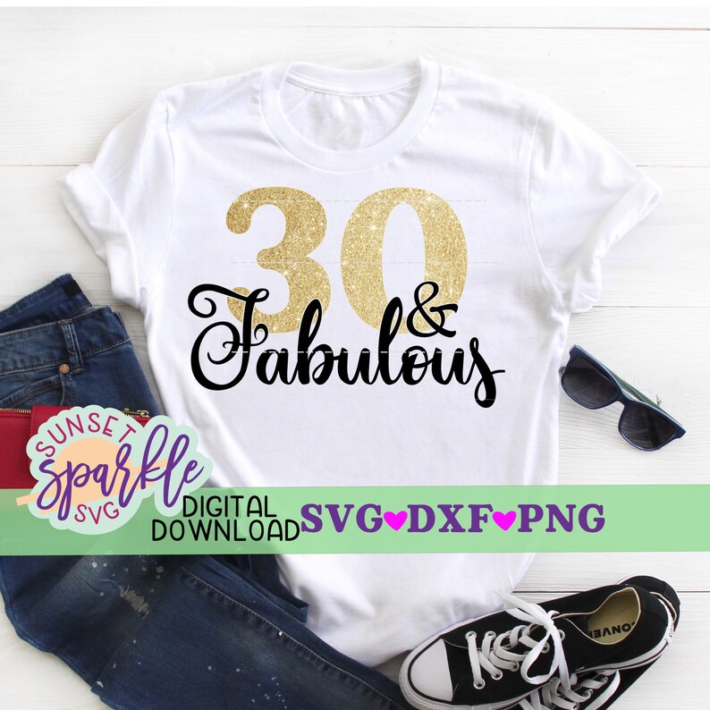 May include: A white t-shirt with a gold glitter number 30 and the text "& Fabulous" in black cursive lettering. The shirt is laid out on a wooden surface with a pair of jeans, sunglasses, and sneakers.