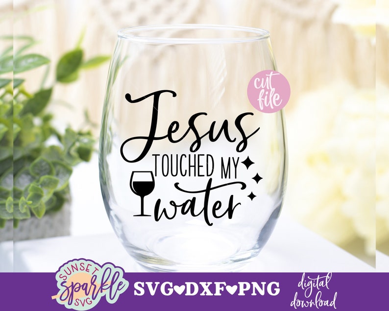 May include: A clear glass wine glass with the text "Jesus Touched My Water" in black lettering. The text is surrounded by small diamond shapes. A small wine glass icon is also included in the design.