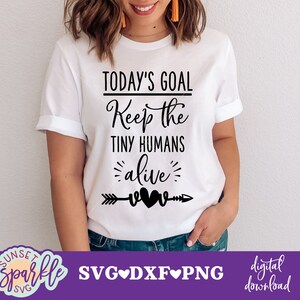 Könnte beinhalten: Weißes T-Shirt mit schwarzem Text, der "Today's Goal Keep the Tiny Humans Alive" lautet, mit einem schwarzen Pfeil und zwei Herzen.