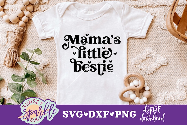 May include: White baby onesie with black text that reads "Mama's little bestie" with hearts around the words.