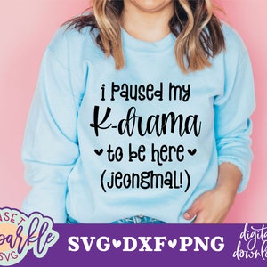 May include: A light blue sweatshirt with the text "I paused my K-drama to be here (jeongmal!)" in black. The text is centered on the sweatshirt. The sweatshirt is on a pink background. The text "SVG DXF PNG digital download" is at the bottom of the image.
