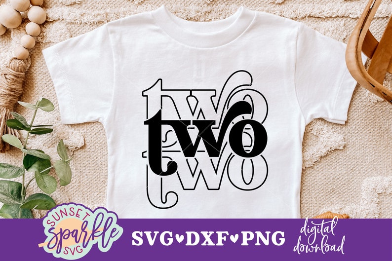 May include: A white t-shirt with a black graphic design that says "two" in a stylized font. The design is surrounded by a decorative border.
