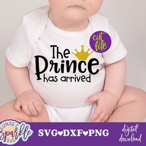 K&ouml;nnte beinhalten: Ein wei&szlig;er Strampler mit dem Text "The Prince has arrived" und einer goldenen Kronengrafik. Der Strampler wird von einem Baby getragen, das auf einer wei&szlig;en Oberfl&auml;che sitzt.