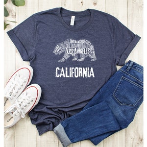 May include: A navy blue t-shirt with a white graphic of a California bear made up of words like "Los Angeles" and "San Francisco". The text "CALIFORNIA" is printed below the bear.