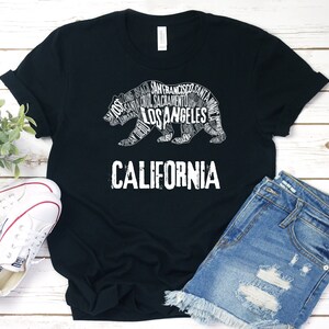 May include: Black t-shirt with a white graphic of a California bear made up of words like "Los Angeles", "San Francisco", and "Sacramento". The text "CALIFORNIA" is below the bear.