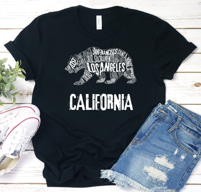 May include: Black t-shirt with a white graphic of a California bear made up of words like "Los Angeles", "San Francisco", and "Sacramento". The text "CALIFORNIA" is below the bear.