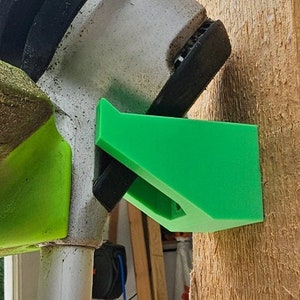 May include: A green plastic wall mount for a weed trimmer or hedge trimmer. The mount is designed to hold the tool securely against a wall.