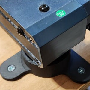 May include: A black electronic device with a green label that says "pass" and a black base with three screw holes.