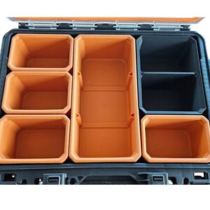 May include: An open black toolbox with orange plastic storage compartments. The compartments are arranged in a grid pattern with a larger compartment in the center.