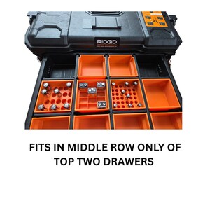 Pode incluir: Caixa de ferramentas preta e laranja Ridgid Pro Gear System com gavetas abertas. As gavetas cont&ecirc;m recipientes de armazenamento laranja com v&aacute;rias pilhas e pe&ccedil;as pequenas. O texto na imagem diz: CABE APENAS NA FILEIRA DO MEIO DAS DUAS GAVETAS SUPERIORES.