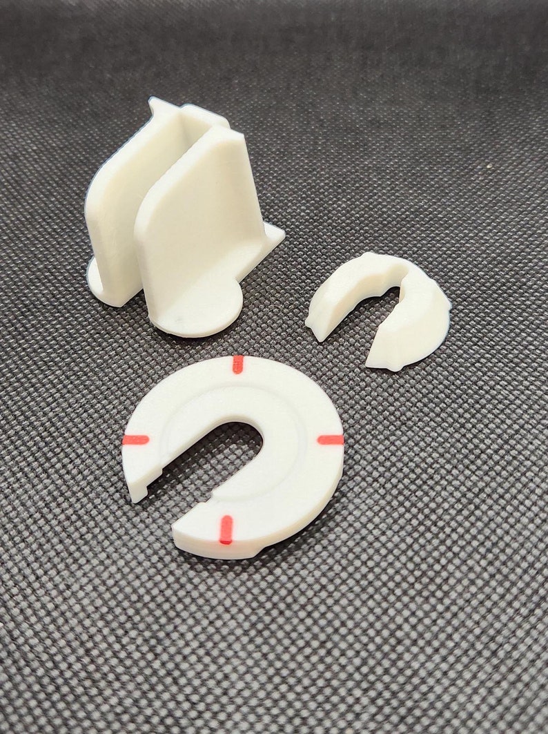Puede incluir: Tres piezas de pl&aacute;stico blanco, dos de las cuales tienen forma de U con un peque&ntilde;o labio en la parte superior, y una es un bloque rectangular con una abertura en forma de U en la parte superior. Las piezas en forma de U tienen marcas rojas en el exterior.