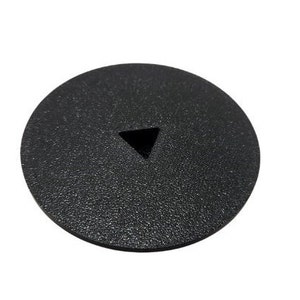 May include: A circular black plastic cover featuring a textured surface and a centered triangular cutout. The object is flat and maintains a consistent dark matte finish across its entire top surface, with the triangular opening clearly visible.