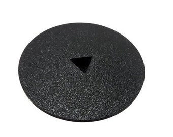 May include: A circular black plastic cover featuring a textured surface and a centered triangular cutout. The object is flat and maintains a consistent dark matte finish across its entire top surface, with the triangular opening clearly visible.