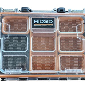 May include: A clear plastic storage box with multiple compartments. The box is orange and black and has the text "RIDGID PRO GEAR SYSTEM GEN 2.0" printed on the top.