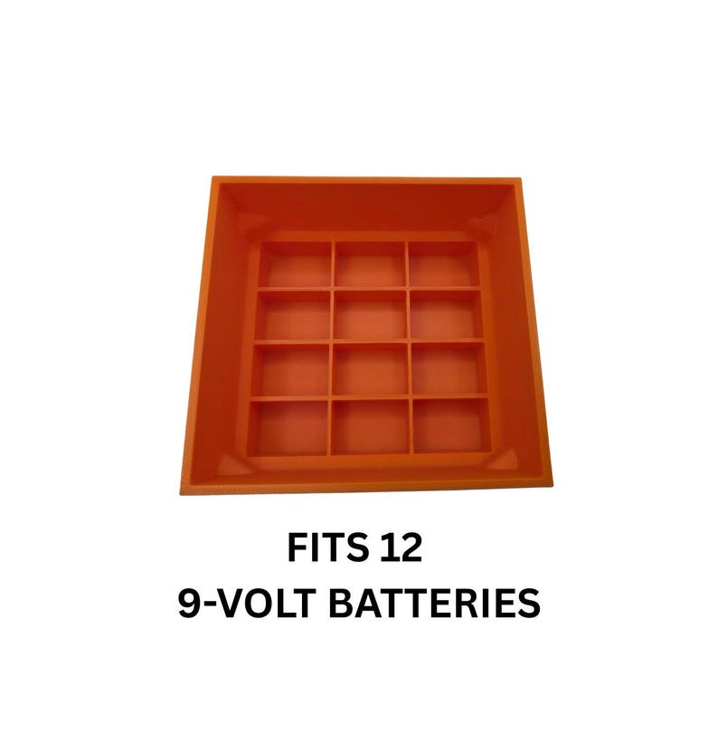Pode incluir: Um organizador de pilhas de pl&aacute;stico laranja projetado para armazenar doze pilhas de 9 volts. O organizador tem formato quadrado com uma grade de compartimentos. O texto "FITS 12 9-VOLT BATTERIES" &eacute; exibido abaixo.