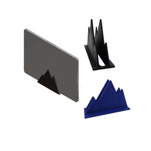 May include: Three mountain-shaped laptop stands in black and blue. One stand is holding a gray laptop. The stands are made of a solid material and have a minimalist design. The stands are designed to hold a laptop upright.