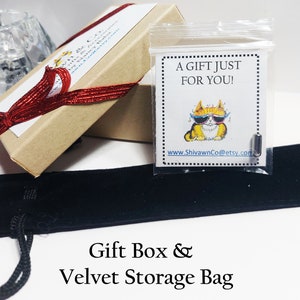 May include: A gift set comprising a small, rectangular item in a clear plastic bag with a cartoon cat graphic and the text "A GIFT JUST FOR YOU!". The set includes a brown gift box tied with a red ribbon and a black velvet storage bag.
